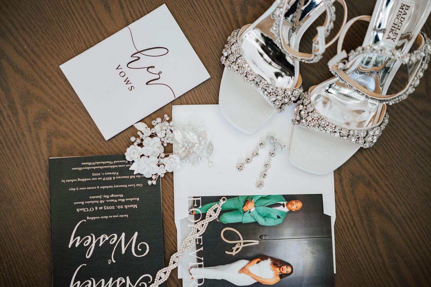 Wedding accessories including sparkly heels, invitation cards, and jewelry arranged on a wooden surface.