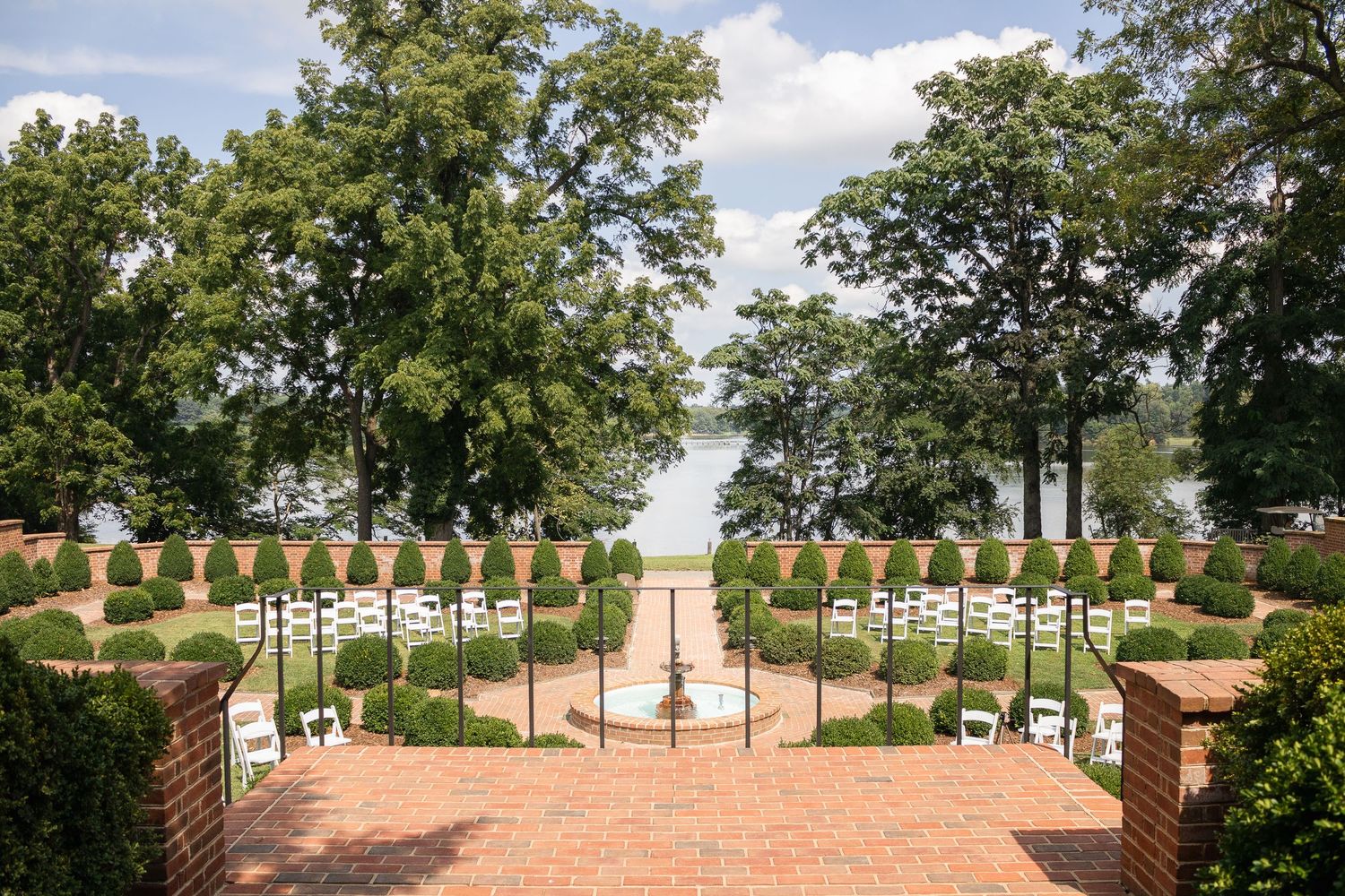 Panoramic view of a formal garden terrace with brick pathways, white columns and lush green trees in summer.