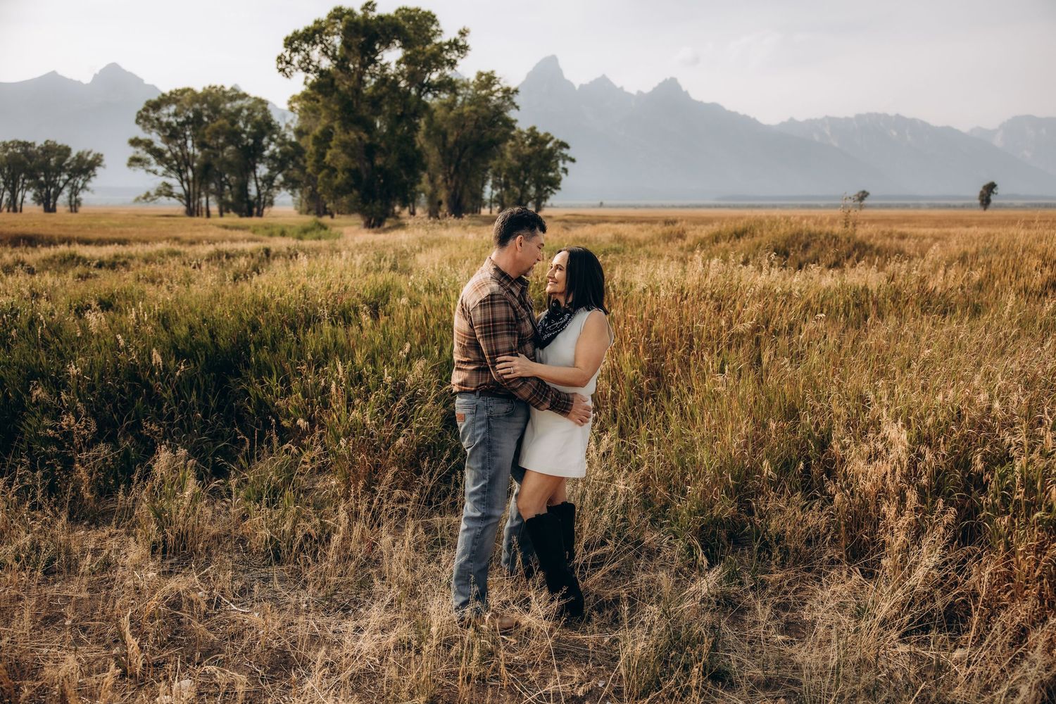 A couple embraces in golden field with mountains in background during sunset creating a romantic silhouette.