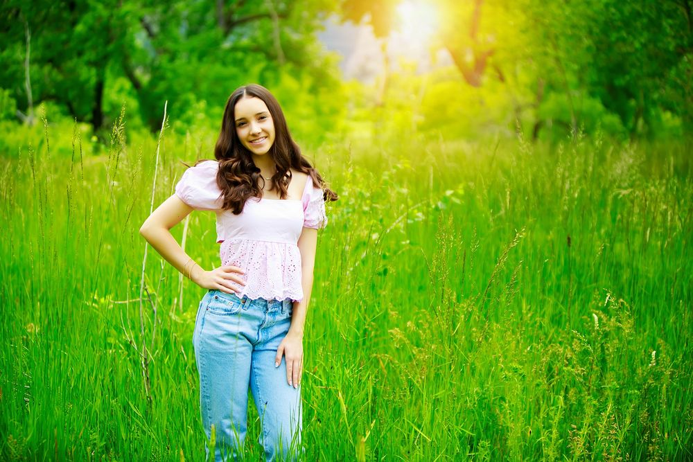 A person in a white t-shirt and jeans stands in a vibrant green summer meadow filled with wildflowers at sunset.