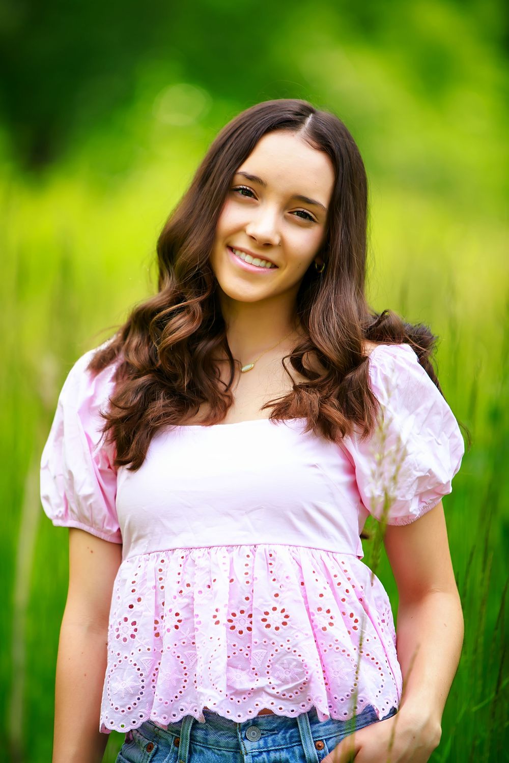 A pink eyelet lace top photographed against a bright green outdoor background.