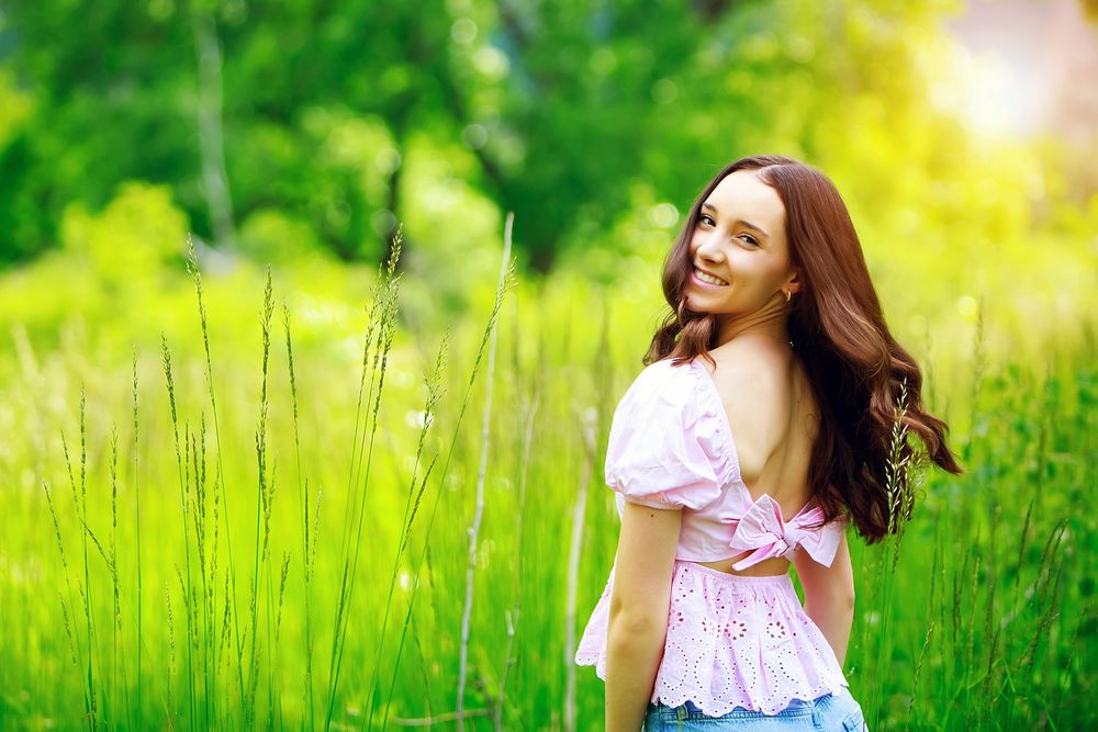 Person in pink dress twirls and dances through a vibrant green summer meadow in bright sunlight.