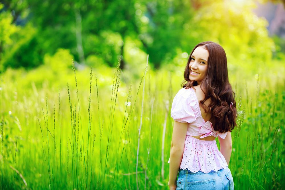 A woman in a floral dress poses gracefully in a lush green meadow at sunset.