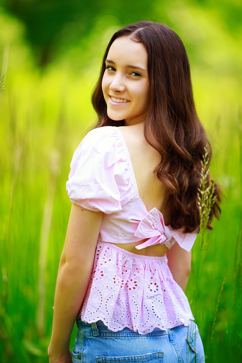 A summer portrait featuring a pink eyelet top and vibrant green foliage background.