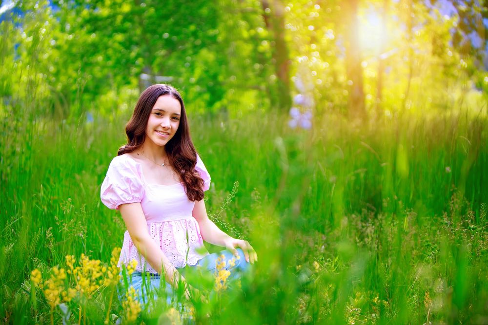 A person in a pink dress sits peacefully in a sunlit meadow with vibrant green grass and yellow wildflowers.