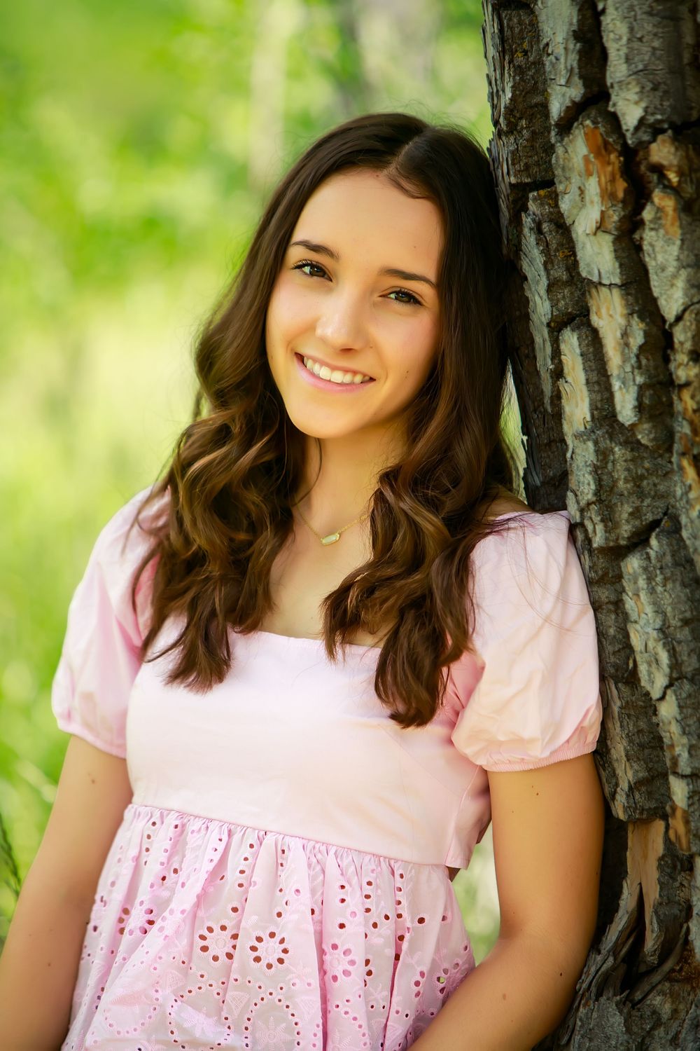 Portrait against a tree trunk wearing a delicate pink blouse with eyelet detailing.