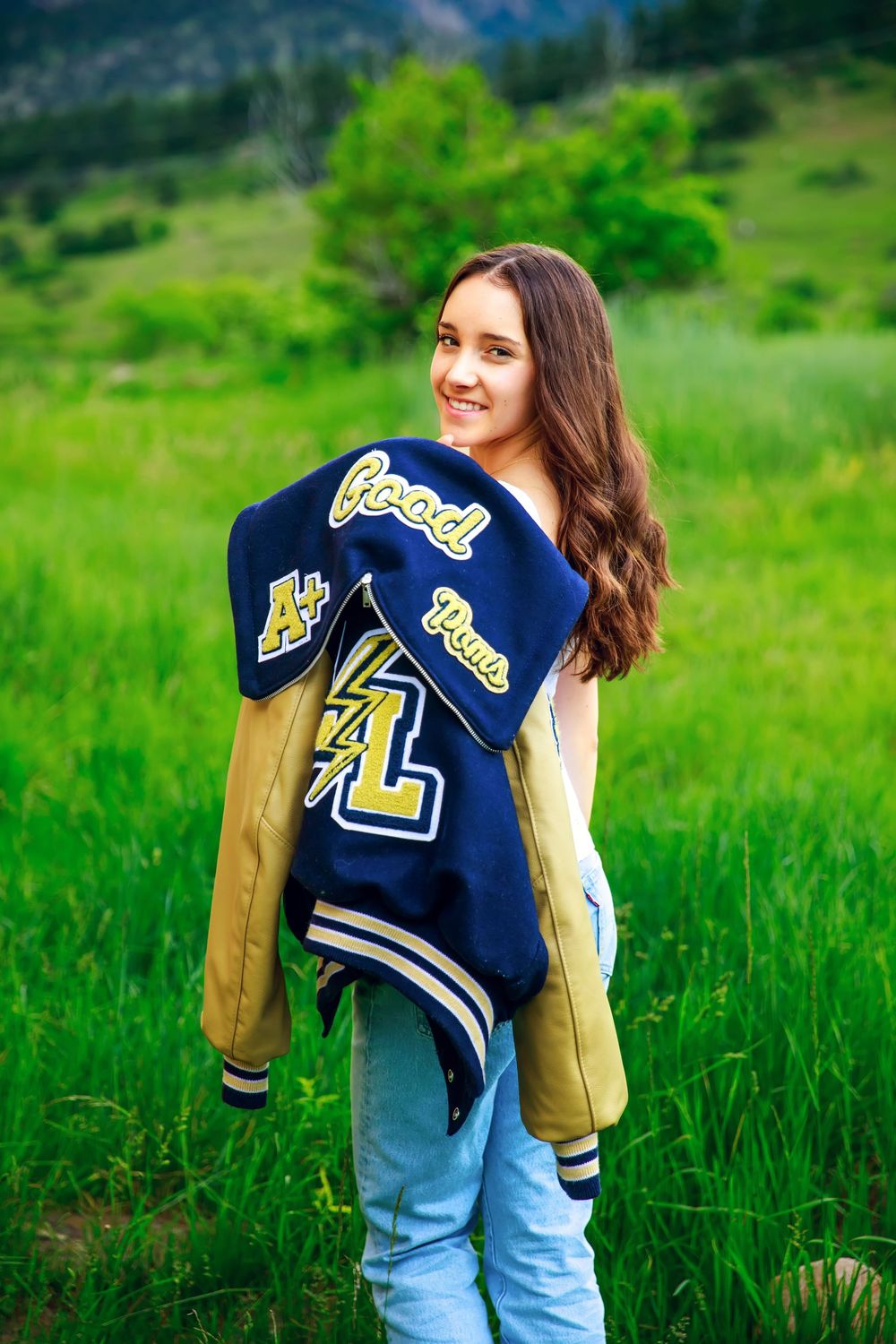 Person wearing a navy and gold varsity jacket poses in a lush green meadow.