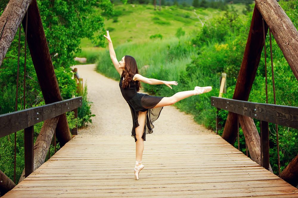 A person in shorts walks across a rustic wooden footbridge through lush green forest scenery.