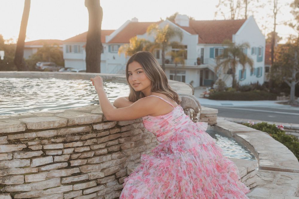 A quinceañera celebration photo session at sunset features a flowing pink ruffled ballgown dress against stone architecture.