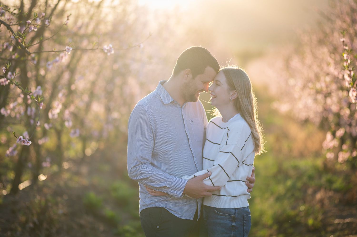 Couple sharing intimate moments together in a golden-lit natural setting at sunset.