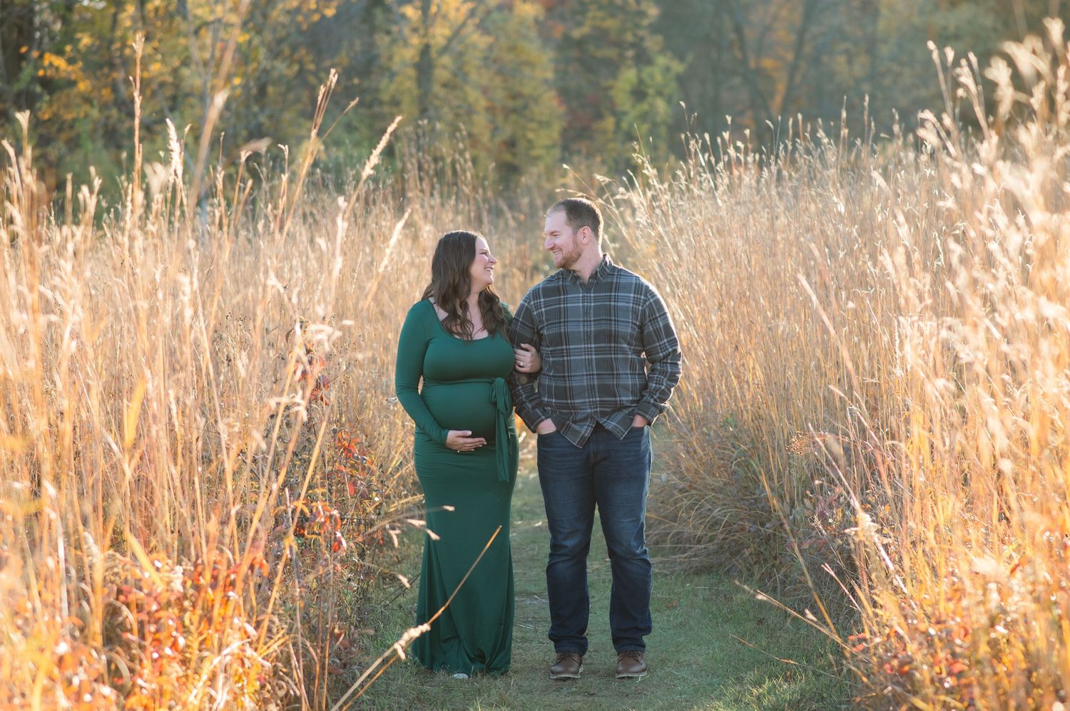 A couple poses together among tall golden grasses at sunset during a fall outdoor photo session.