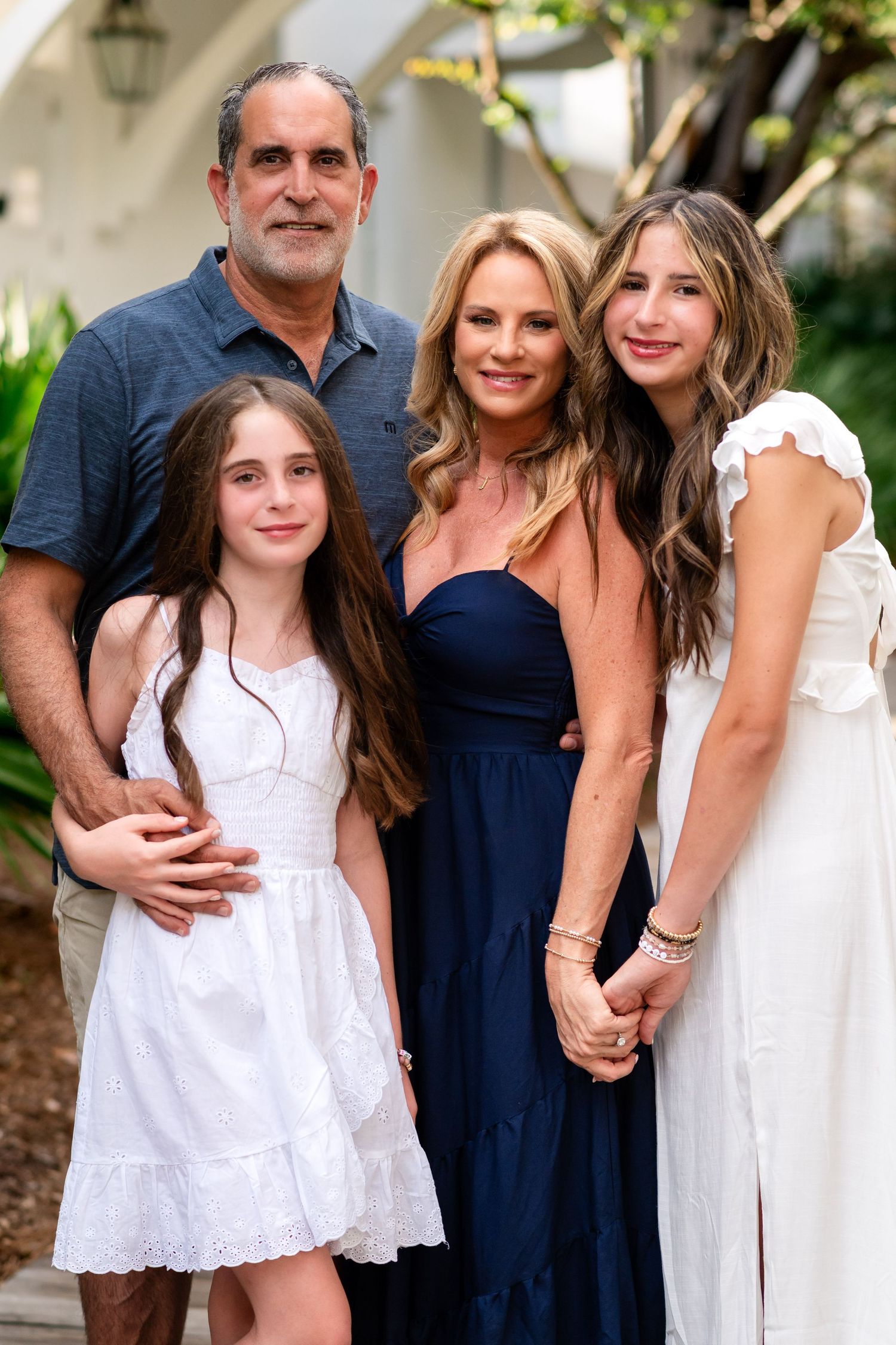 A family in coordinated white and navy outfits poses together outdoors against a garden backdrop.