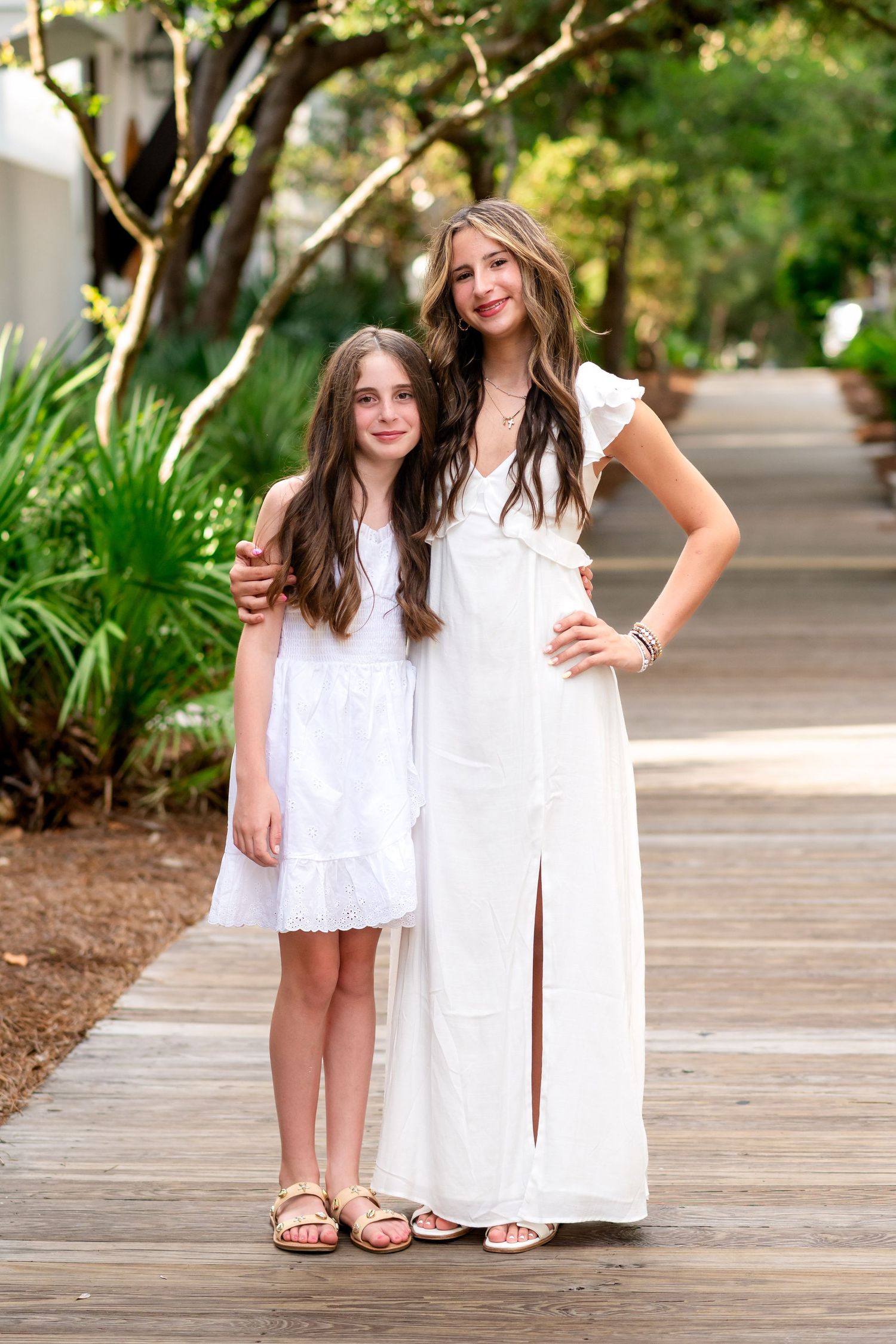 People in white dresses standing together on a wooden boardwalk surrounded by lush greenery.