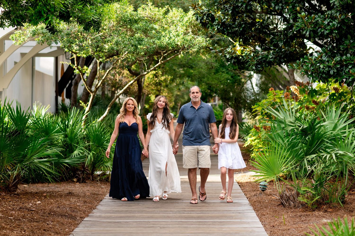 Group walking along a lush garden path surrounded by tropical plants and palm trees on a sunny day.