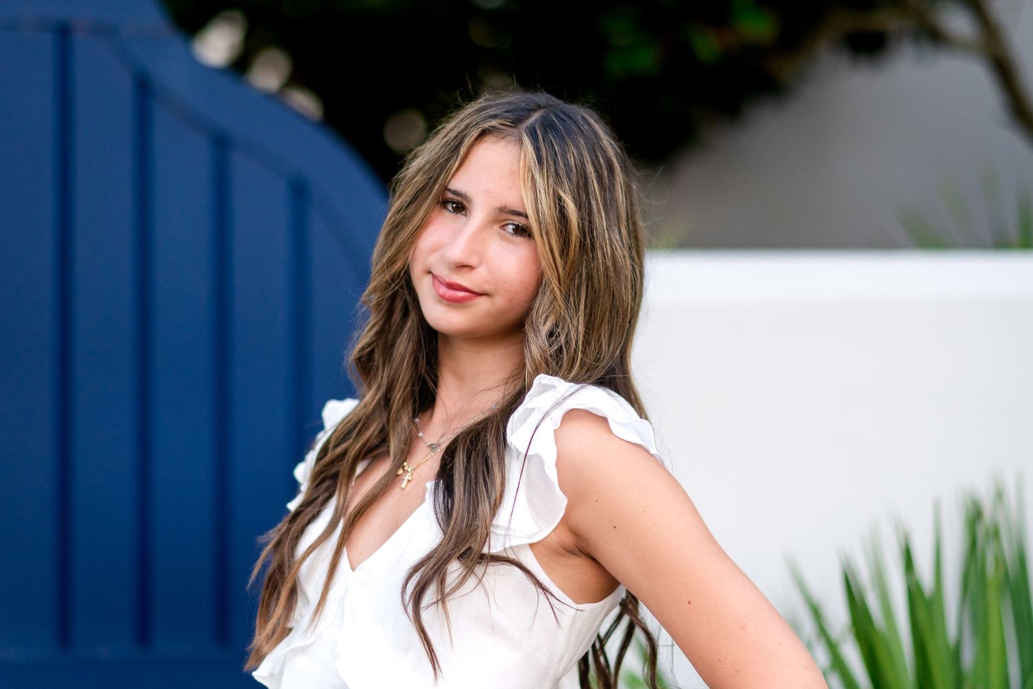 People in coordinated blue and white casual attire pose by tropical plants and navy blue walls.