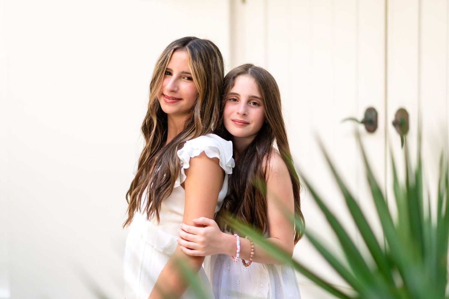Friends wearing coordinated white and navy outfits embrace while standing against a white wall with palm plants.