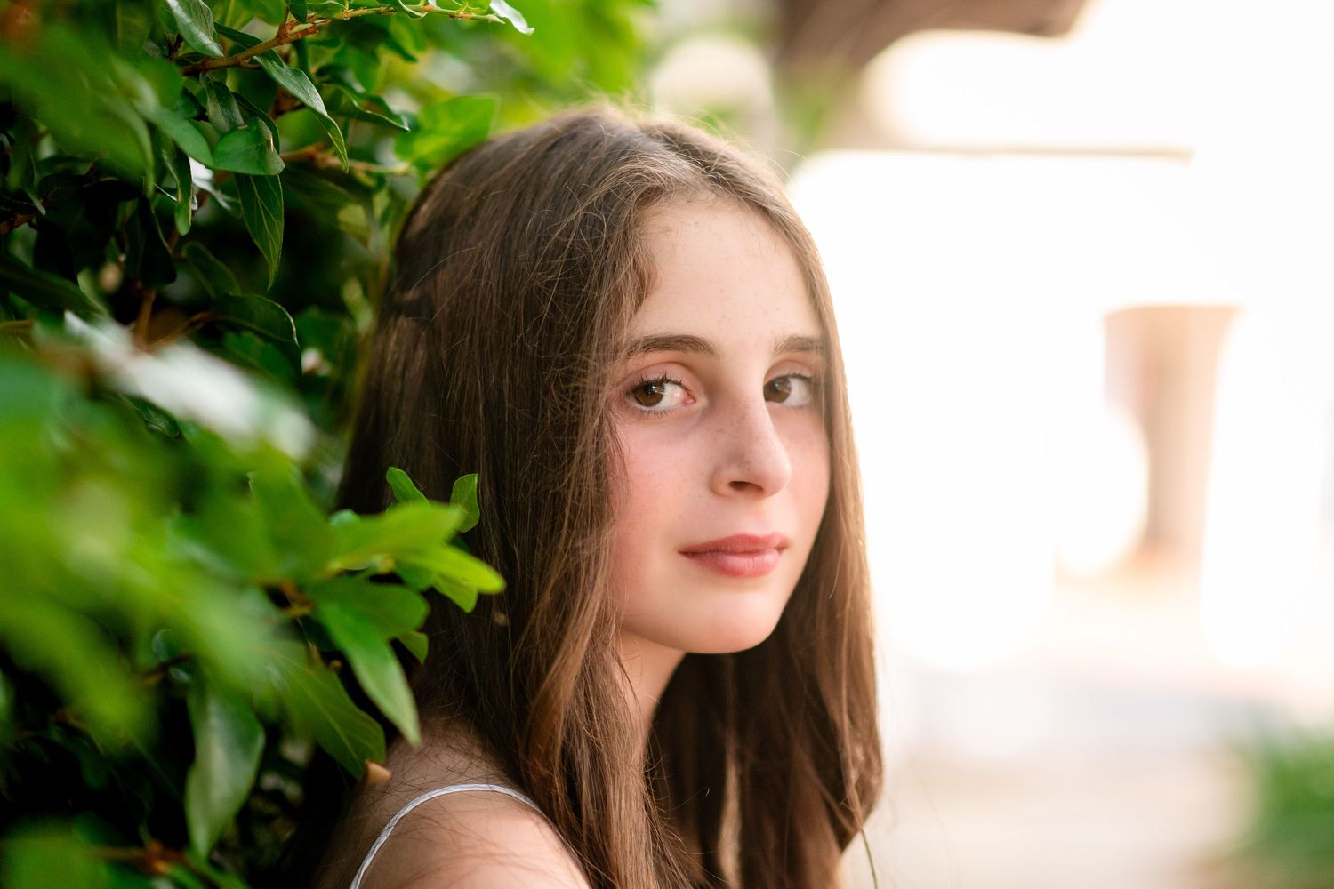 A figure in casual attire poses against a vibrant green foliage background in natural lighting.
