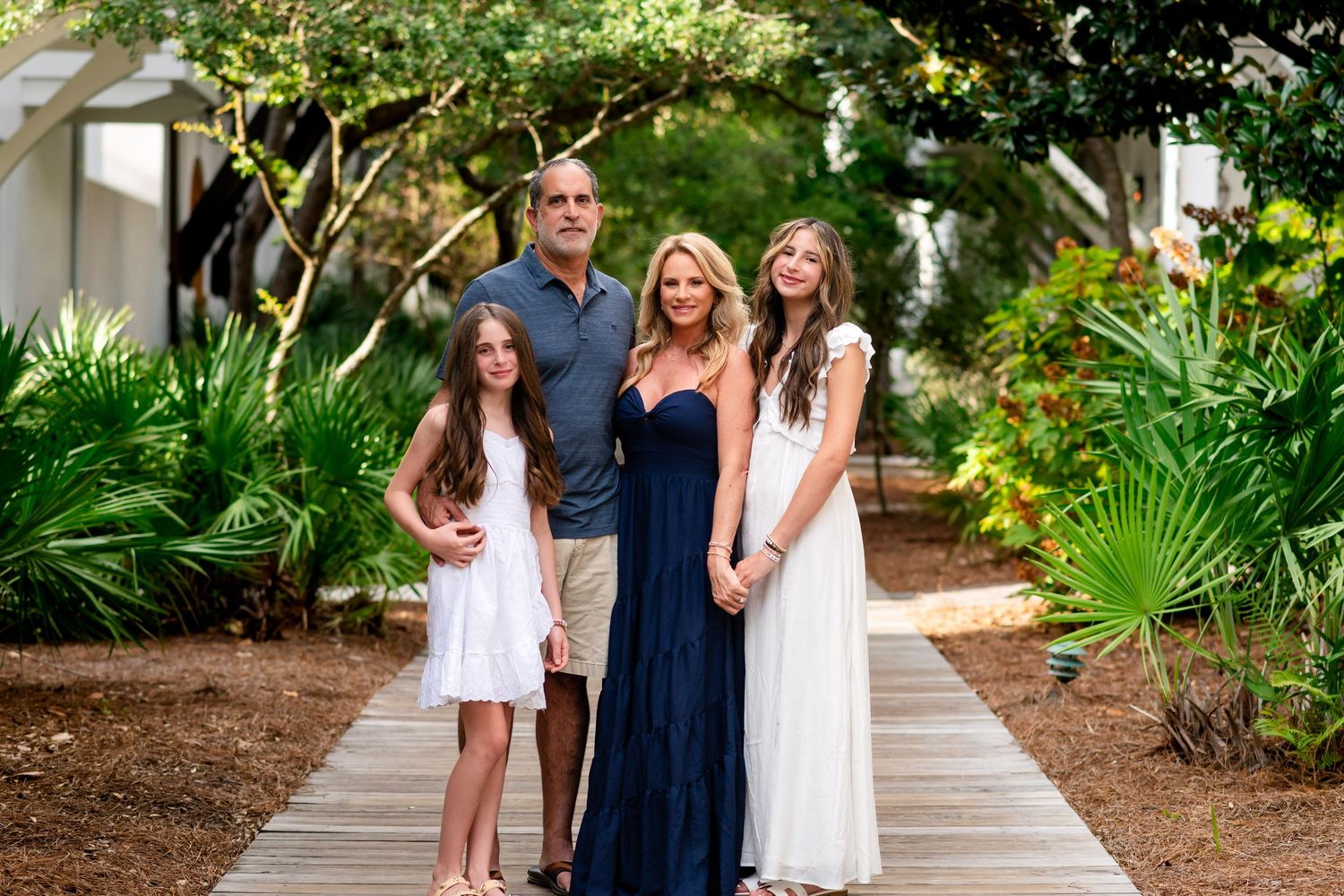 Three people in coordinating blue and white outfits pose together in a lush tropical garden setting.