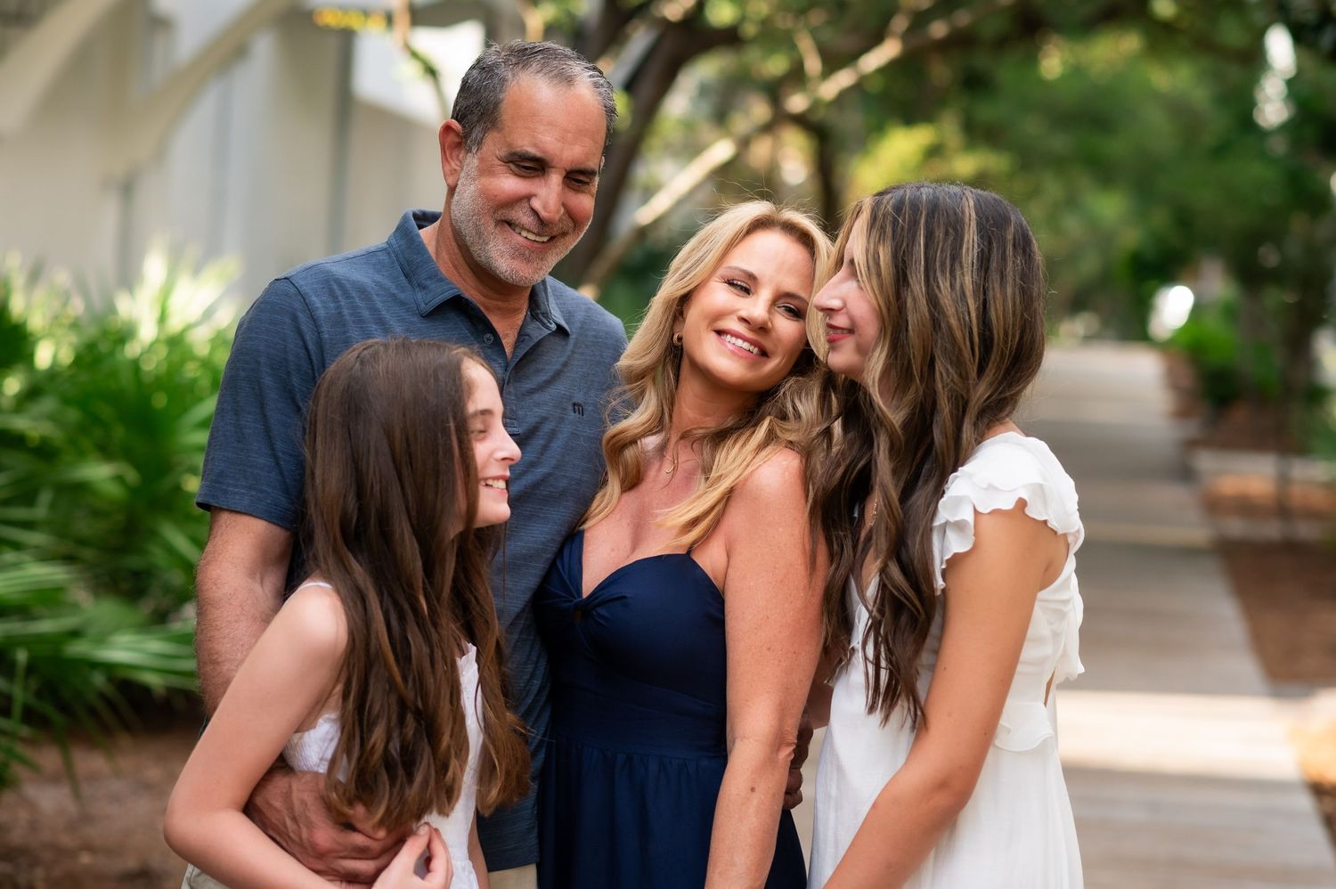 A family of four sharing a candid laughing moment together outdoors on a sunny day.