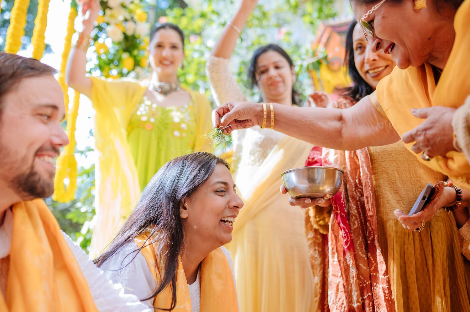 Bride and groom covered in turmeric during an Indo-Norwegian wedding and Family applying Haldi to the bride during a joyful wedding ritual