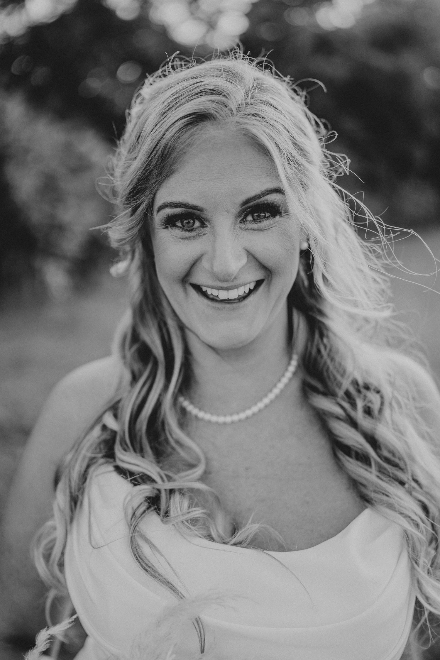 Black and white portrait featuring natural light, blonde curls, pearl necklace, and a joyful expression.