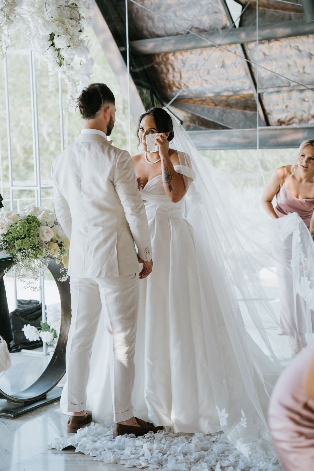 Wedding couple in all-white attire share intimate moments in bright indoor setting.