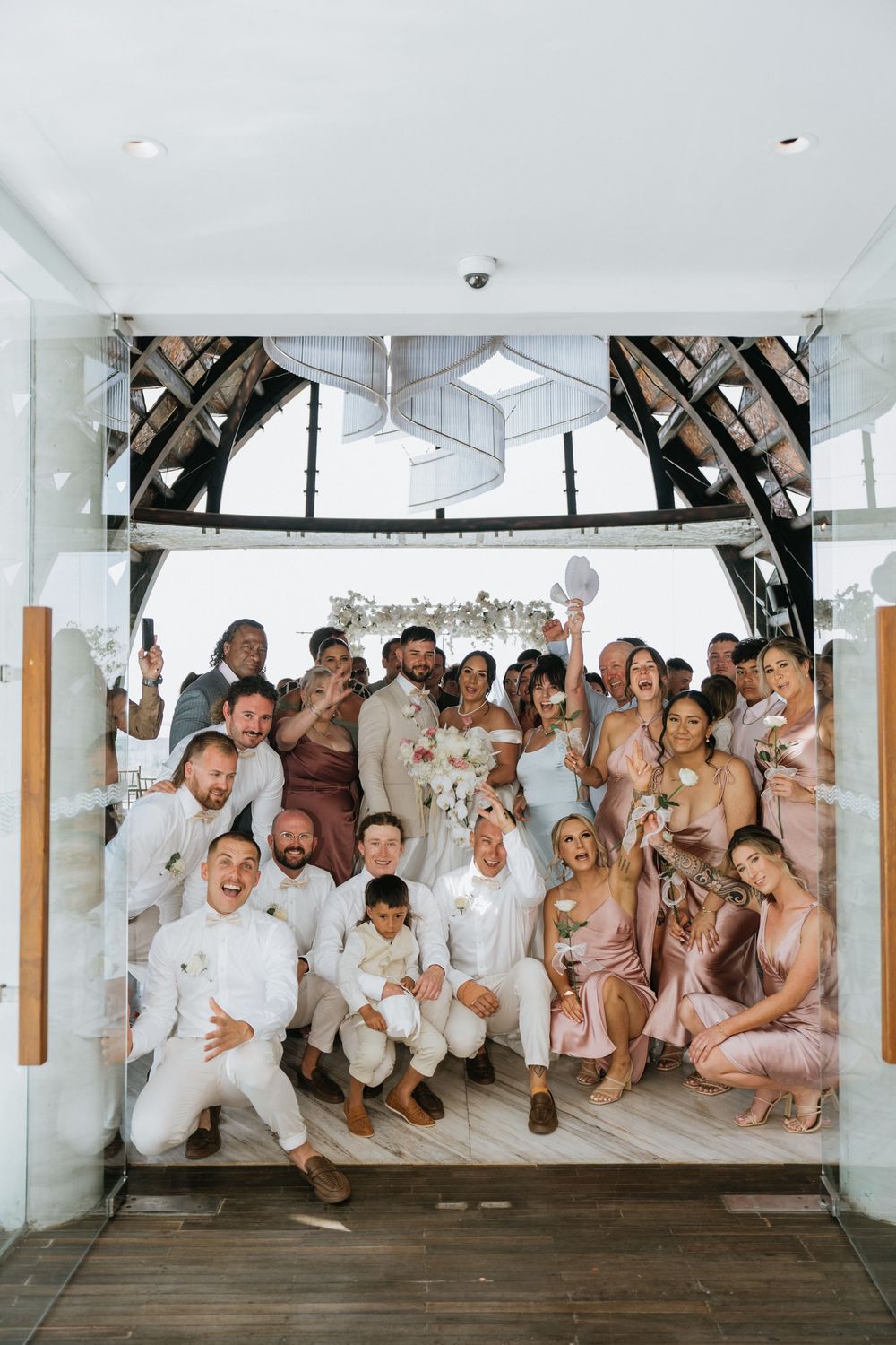 Wedding party in white and blush outfits poses playfully for group photo.
