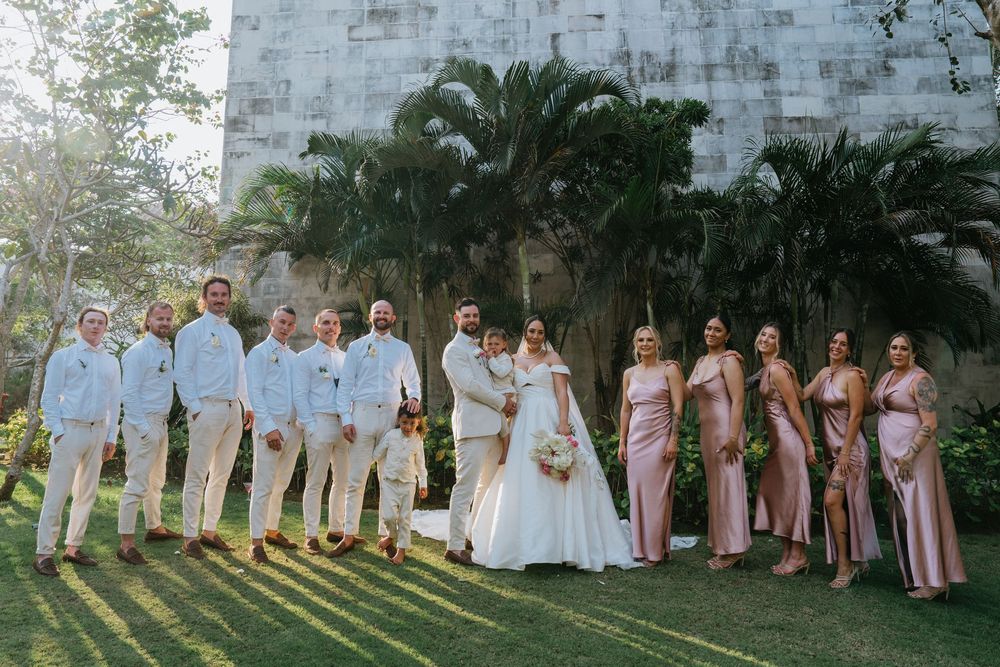 Wedding party members in pink and white dresses pose together in garden setting.