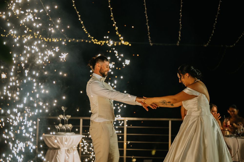 Wedding party dances under twinkling string lights during evening reception celebration.