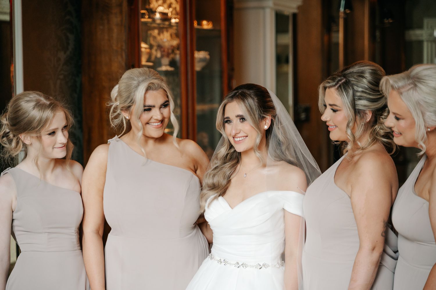 Row of bridesmaids in soft neutral dresses standing together at wedding ceremony.