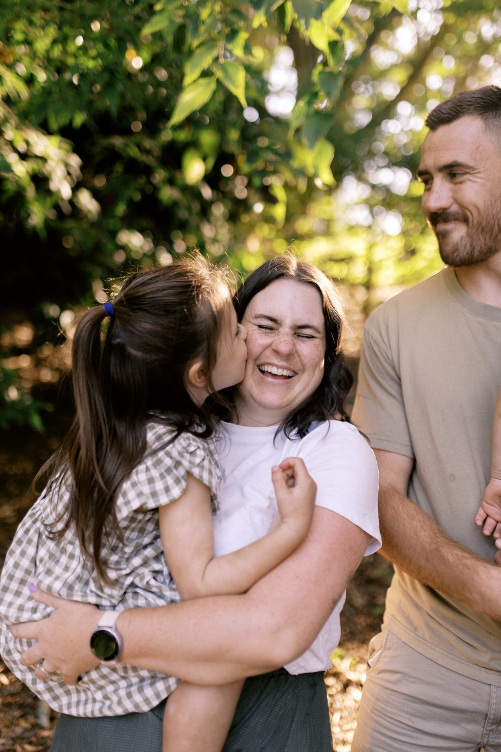 A family embraces and laughs together during an outdoor photo session among green foliage.
