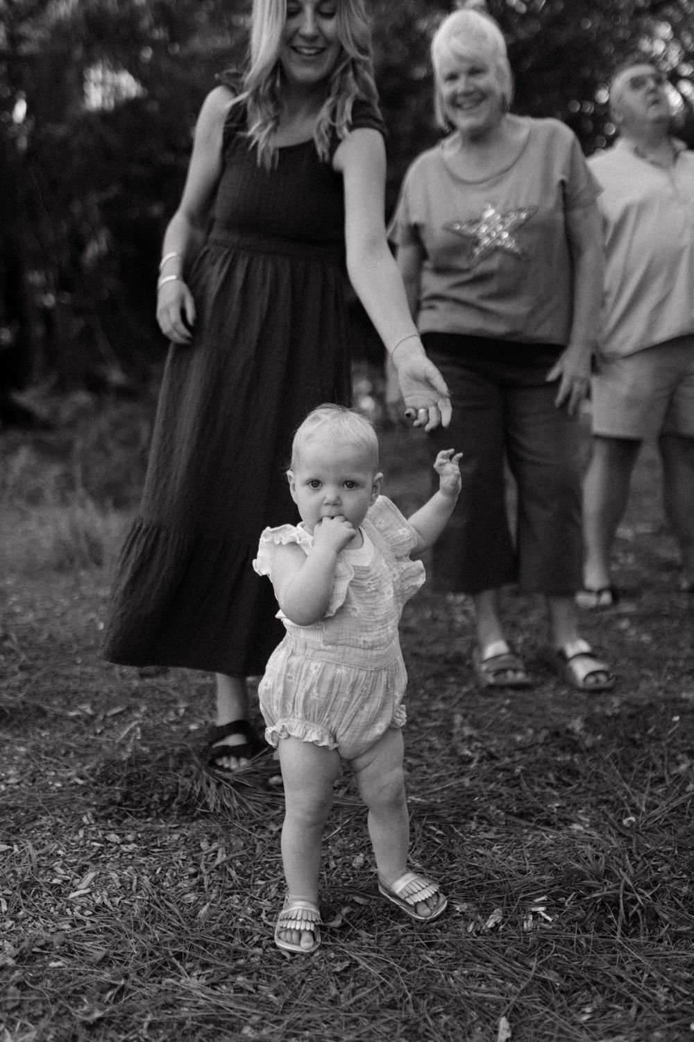 Black and white series showing a baby in a white ruffle outfit taking first steps outdoors.