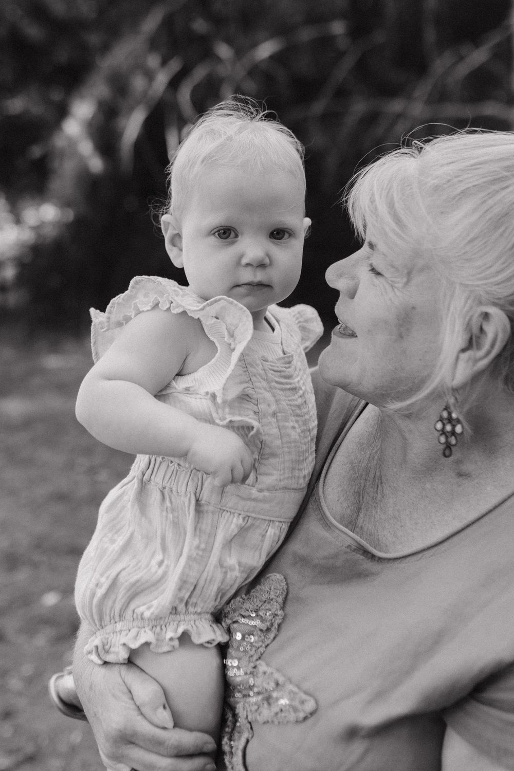 Black and white images of a baby in white ruffled clothing being held lovingly.