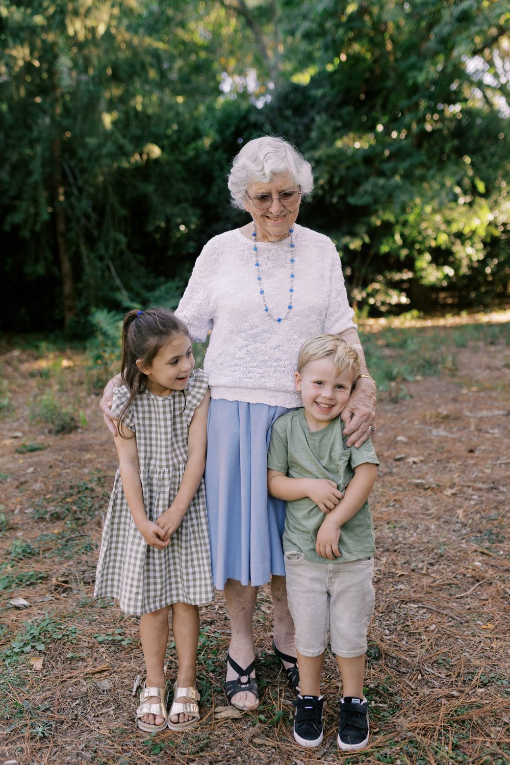 A heartwarming family portrait taken outdoors showing sweet interactions between children and elderly figure.