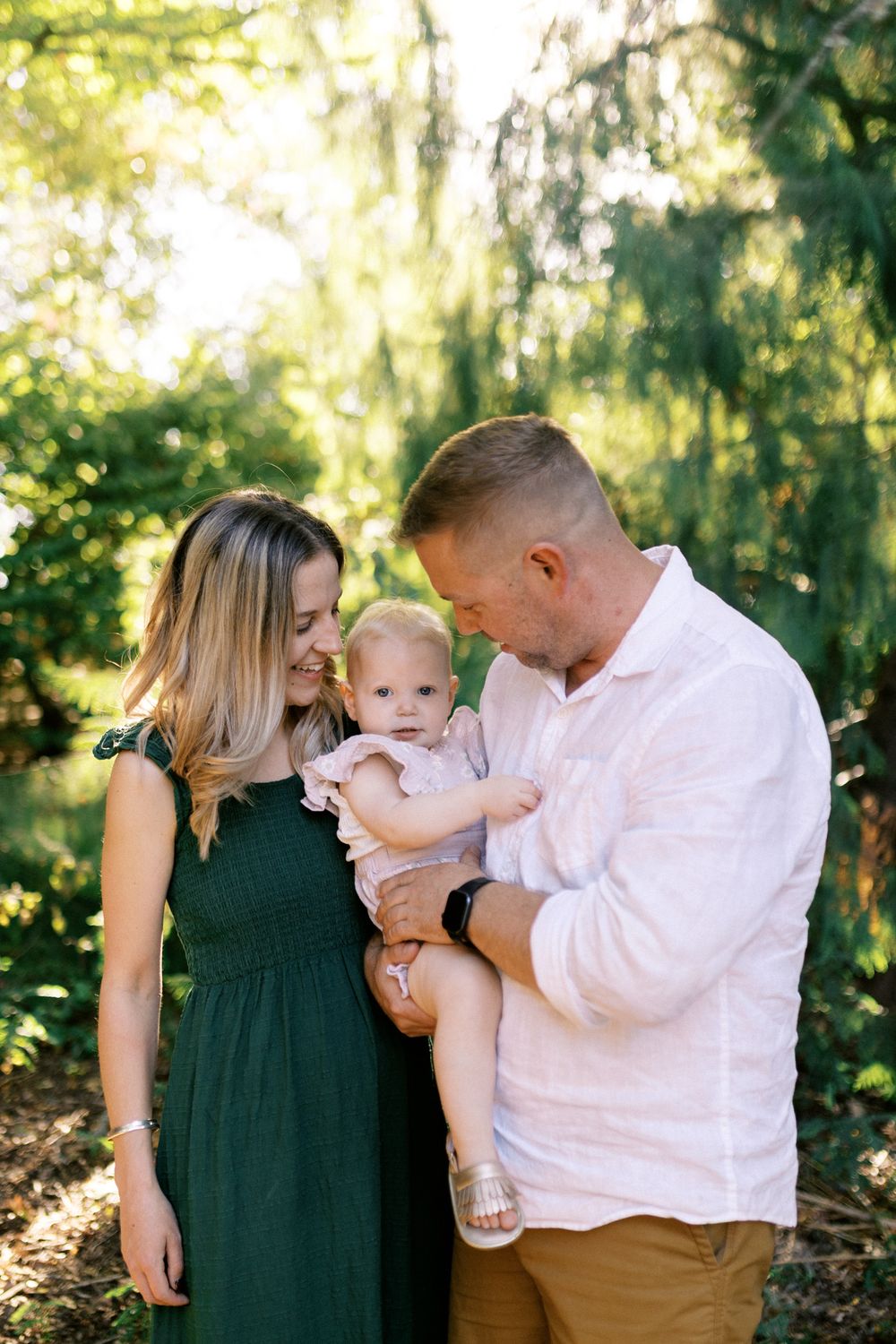 Family portrait series showing sweet interactions in a sunlit forest setting.