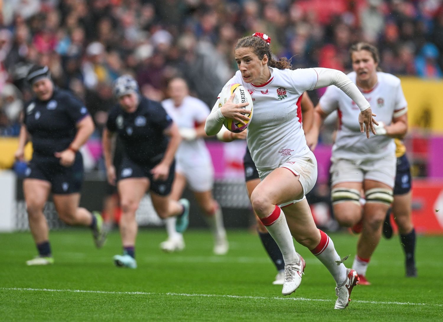 Rugby player carrying ball during match dives towards try line on grass field during competitive game play.