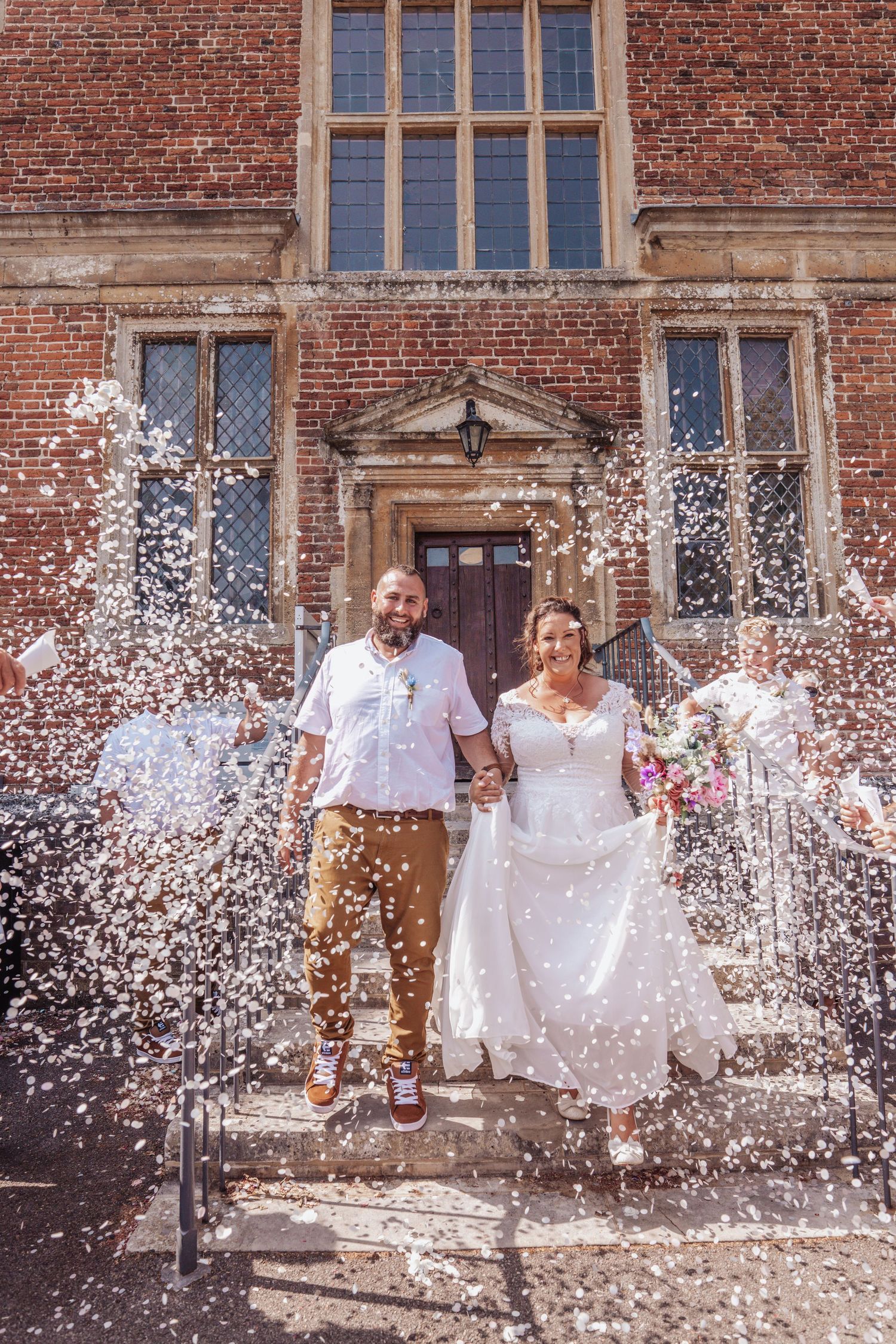 Wedding celebration with confetti shower in front of historic brick building.