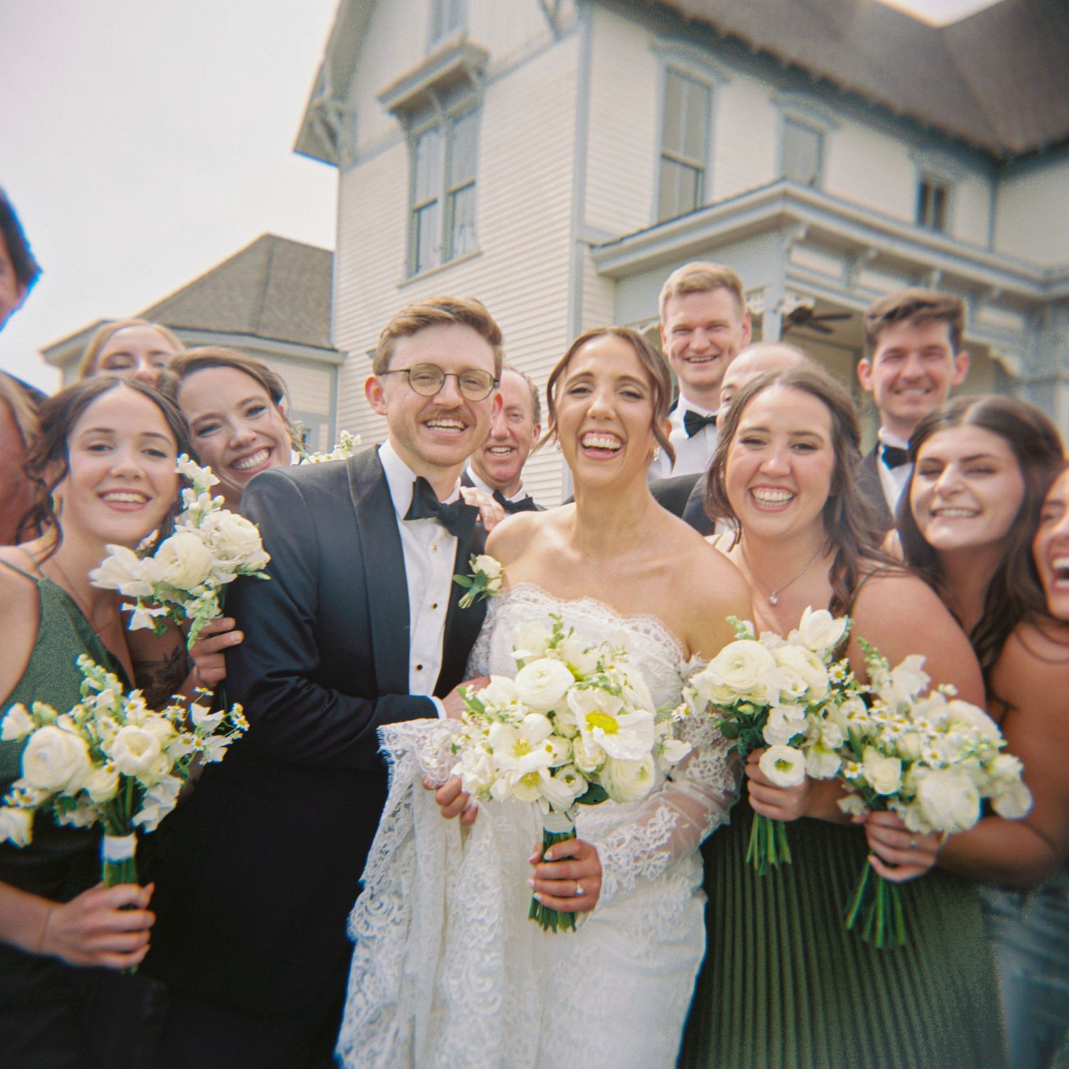 Joyful wedding party celebrating with bride and groom outside historic venue.