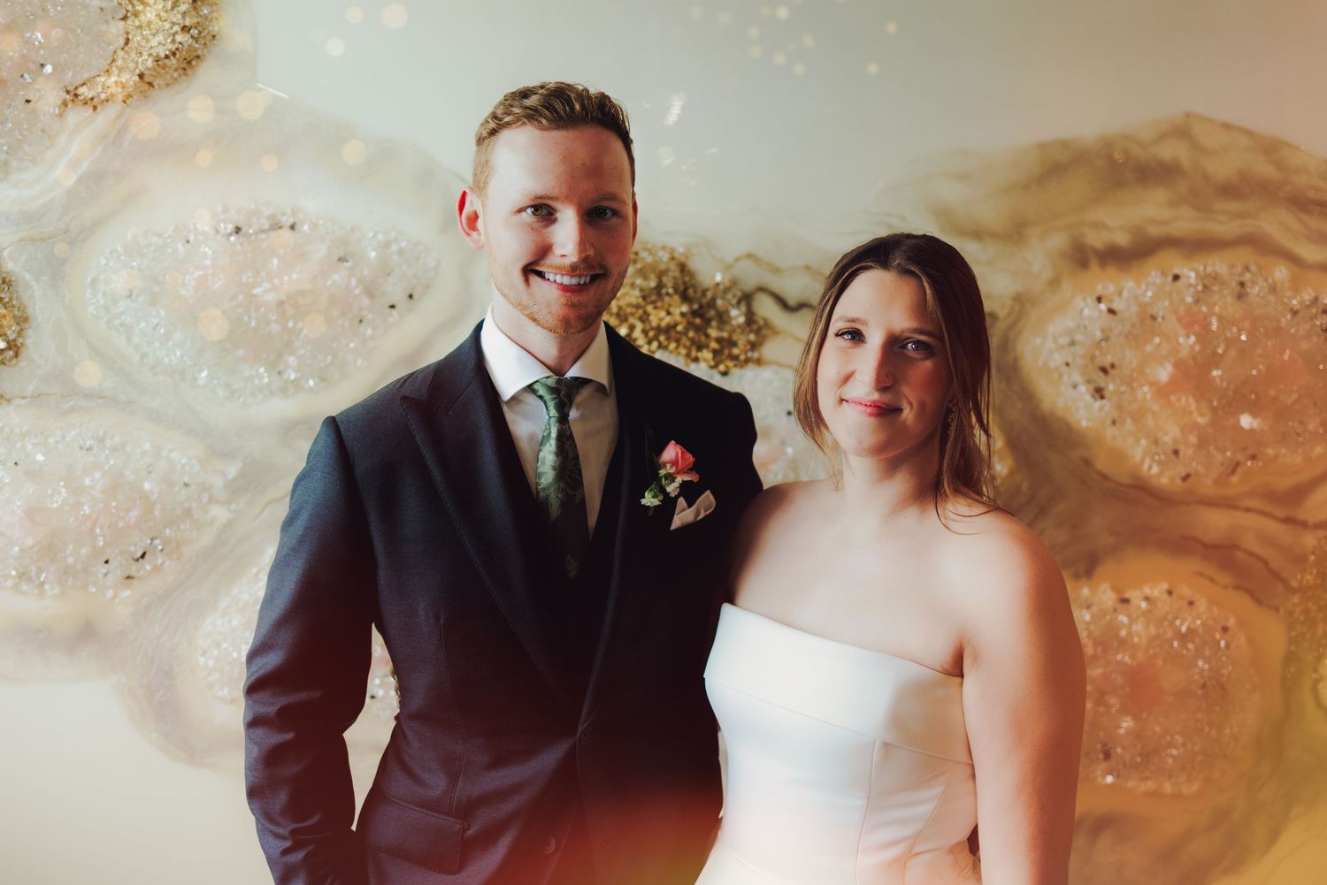 A couple in formal wedding attire sits together against a blurred neutral background during their wedding day.