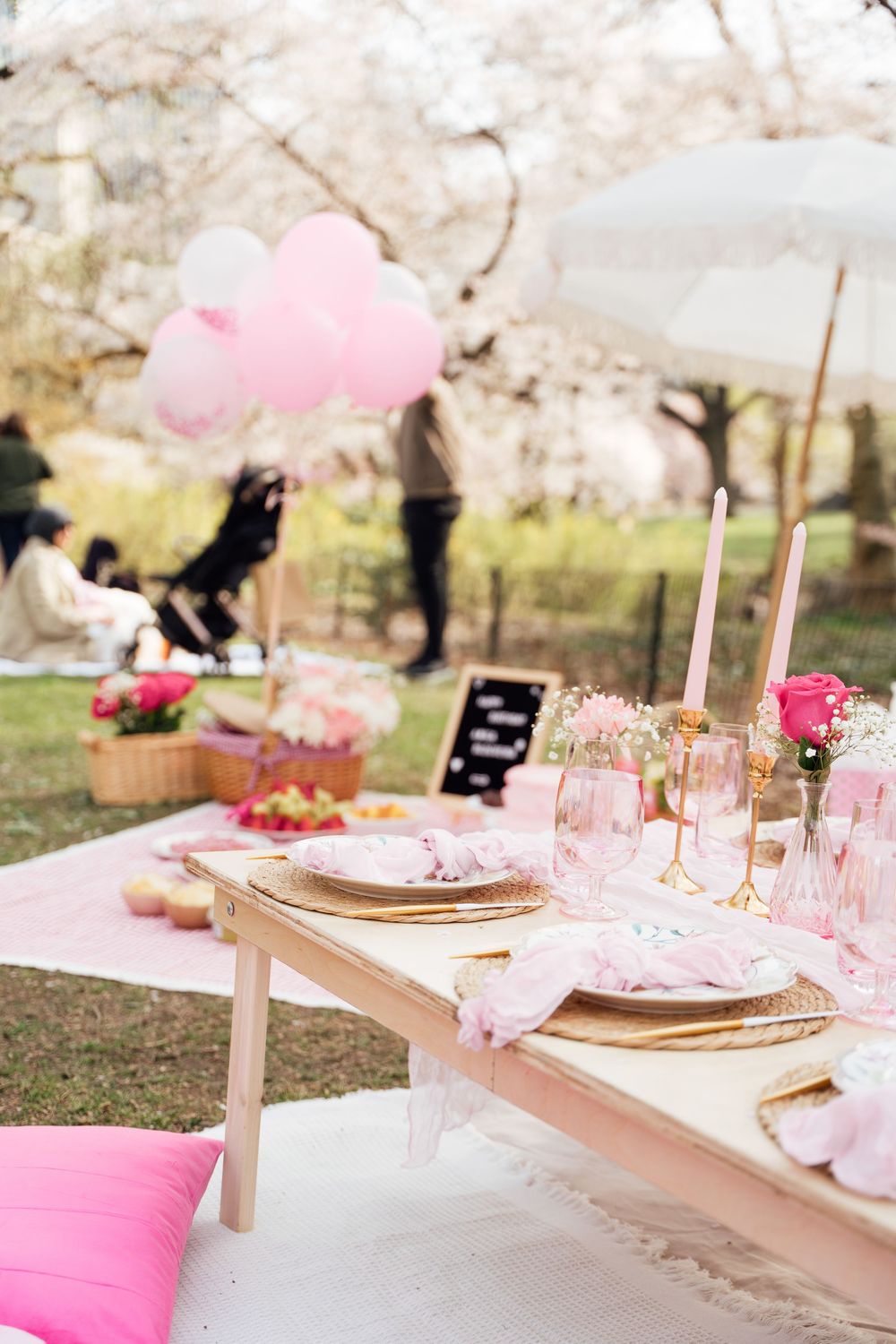 Pink and gold table settings with cherry blossoms create an elegant outdoor dining scene under blooming spring trees.