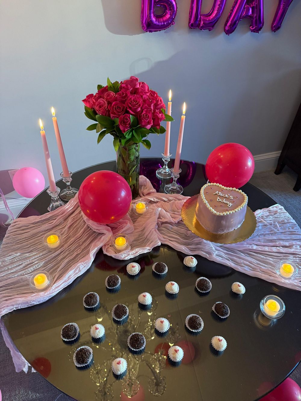 A festive birthday table setup with balloons, red roses, and small dessert glasses arranged in a row.