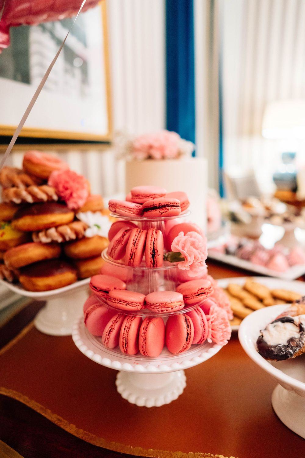 Pink macarons are elegantly stacked on a white cake stand at a dessert table display.