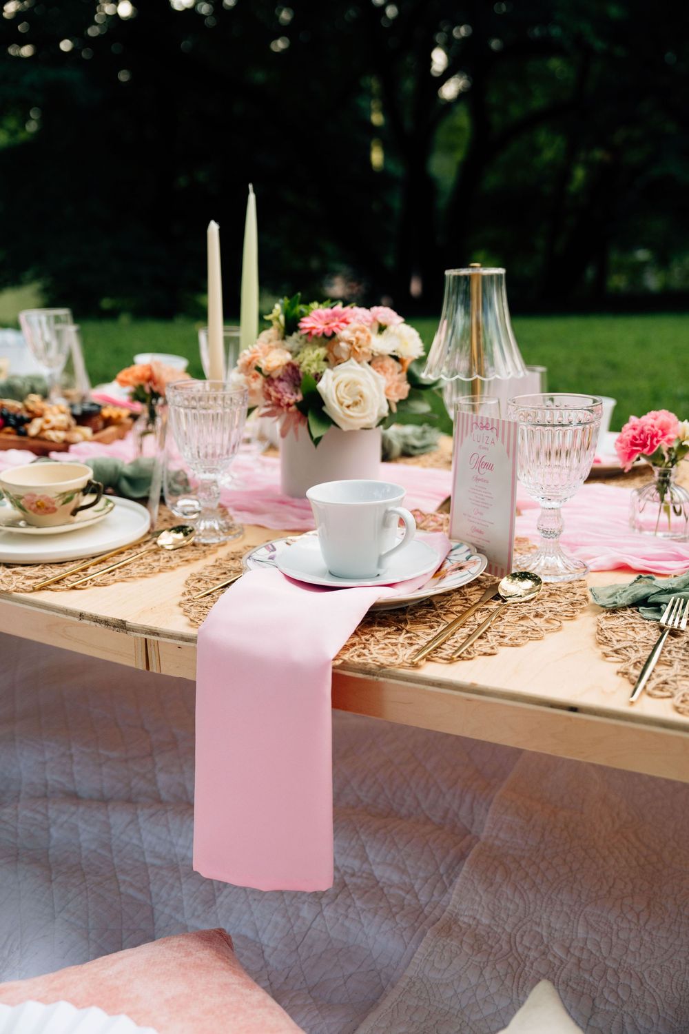 Elegant pink and gold table setting with flowers, candles and place settings for an outdoor garden party celebration.
