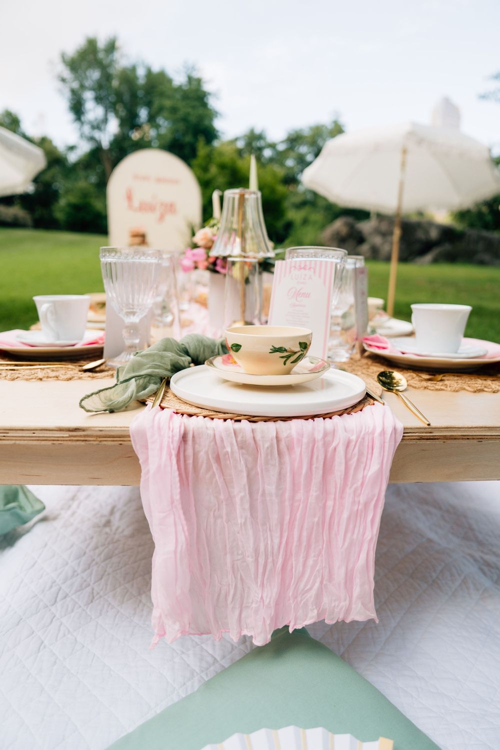 Elegant white place settings on a wooden table with pale pink linens and soft decor create a romantic tablescape.