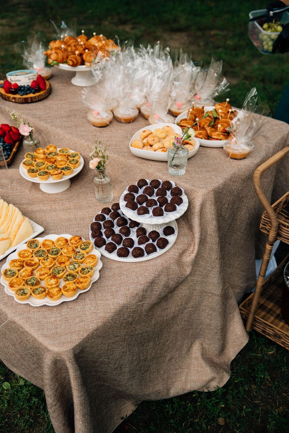 Elegant dessert table covered with burlap cloth displays chocolate truffles, canapes, and appetizers at an outdoor event.