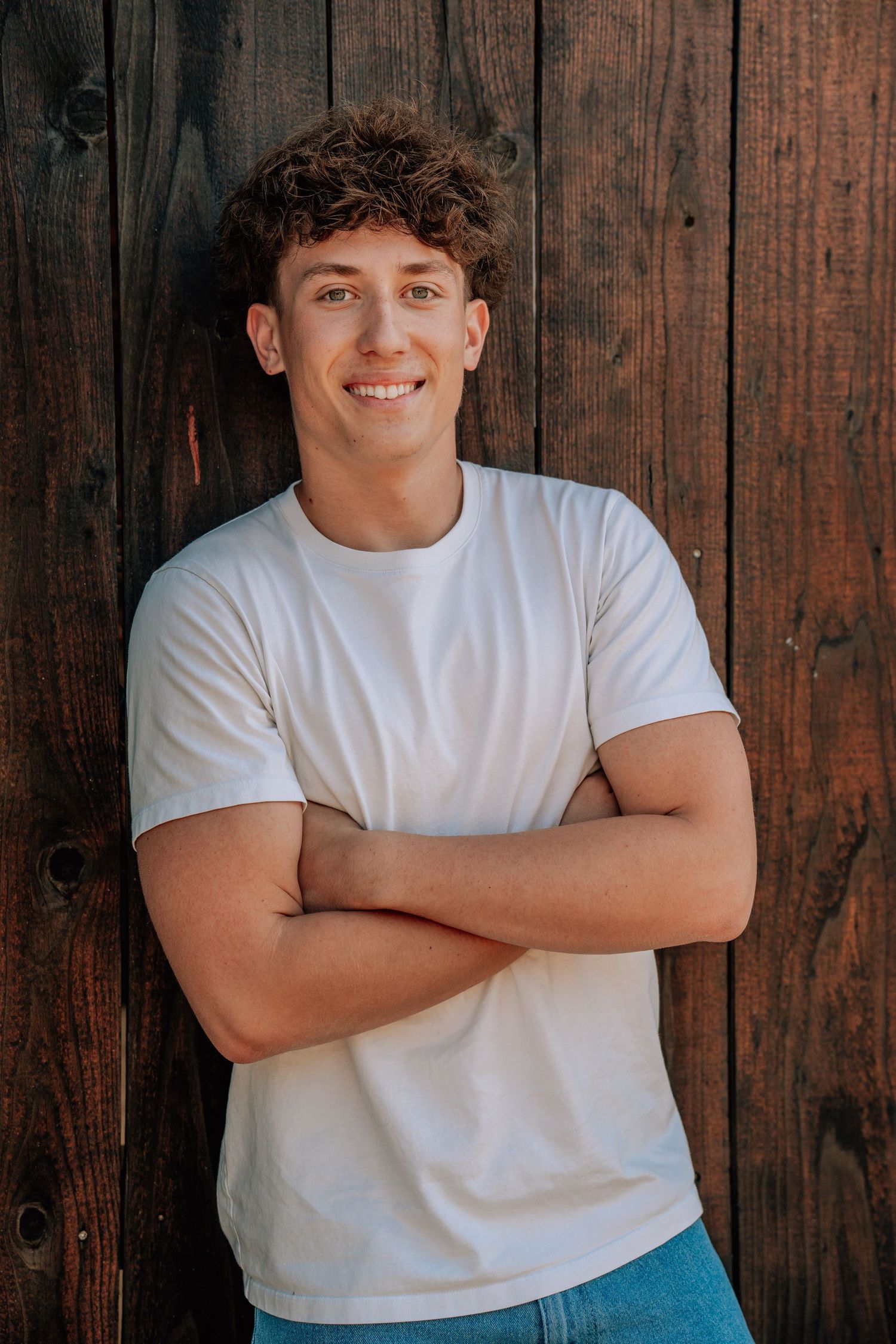 Young man in white button-down shirt poses against rustic metal wall background.
