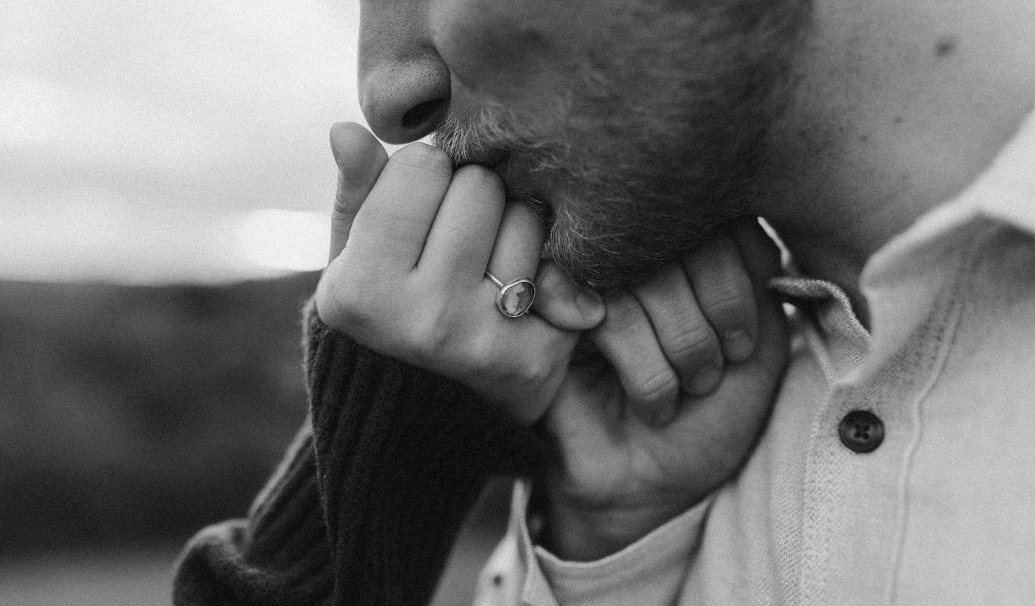 Close-up black and white photo showing hands and an engagement ring.