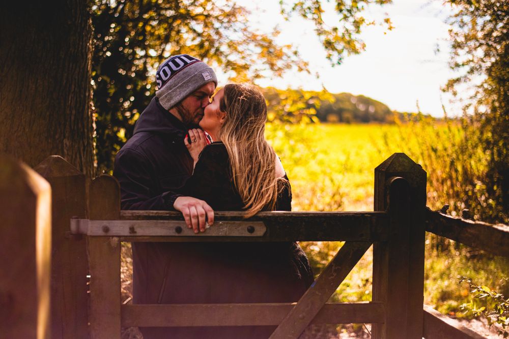 A couple shares a romantic moment leaning against a wooden fence at sunset.