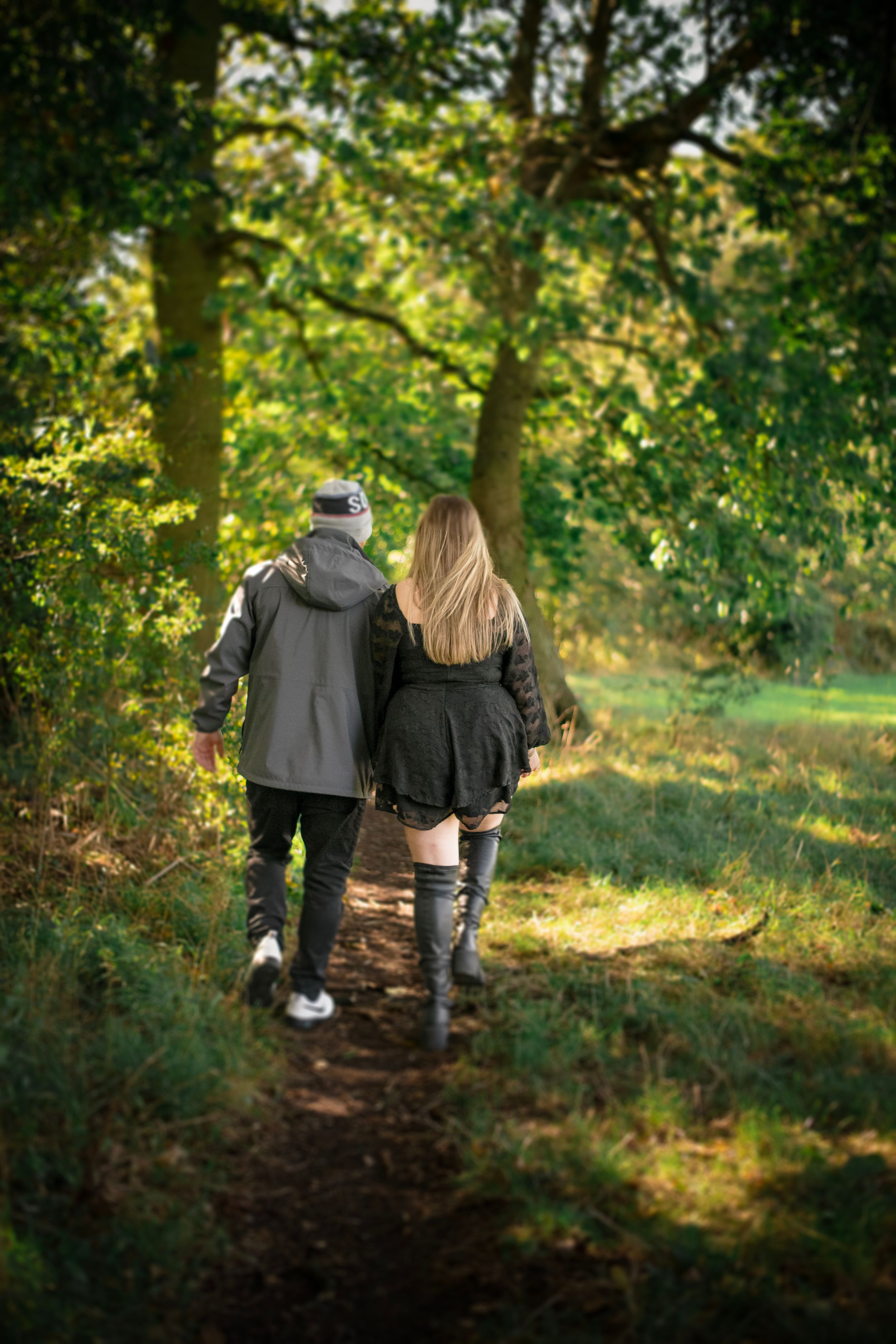 A couple walks together on a wooded path during golden hour.