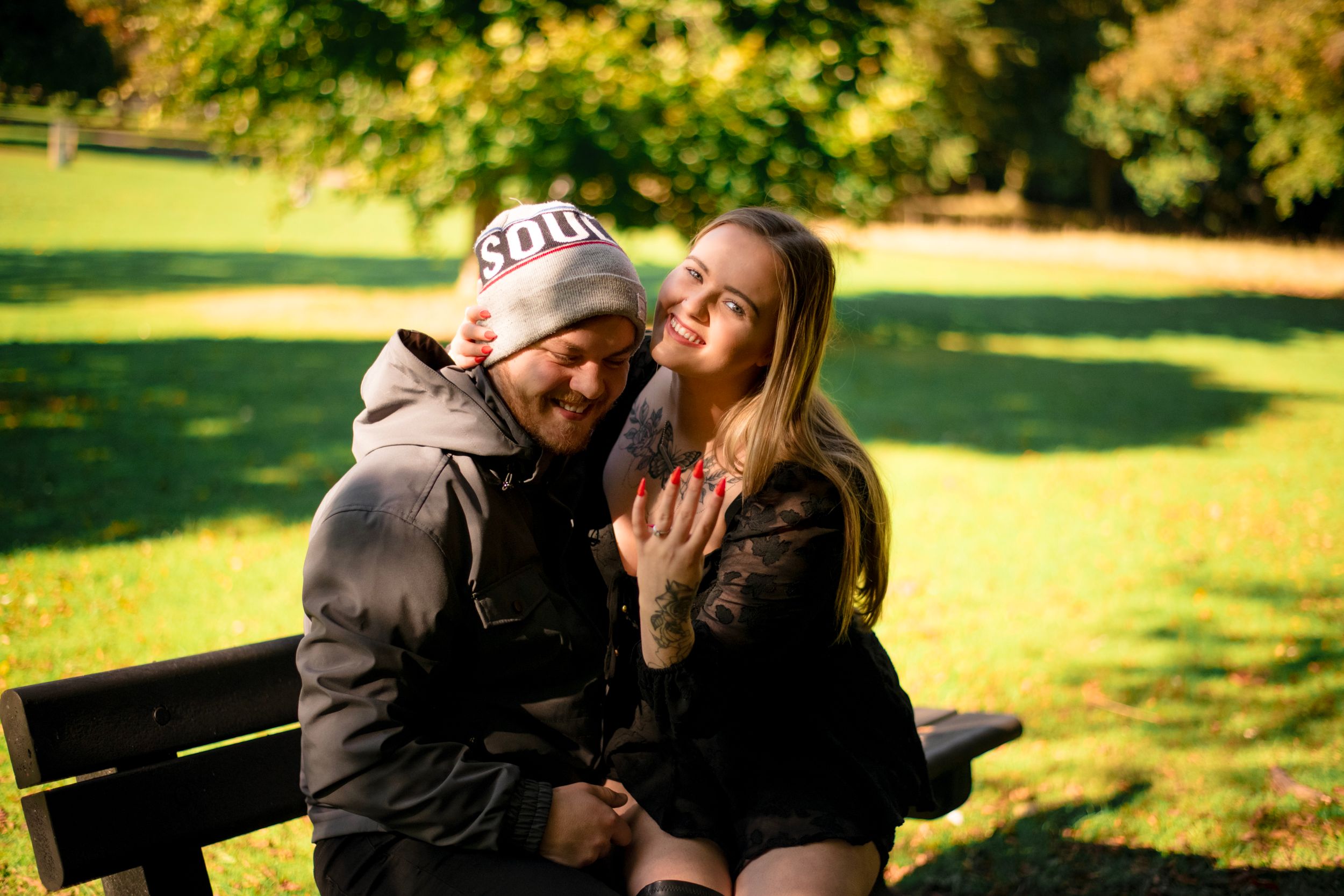 A happy couple sits together on a park bench surrounded by autumn foliage.